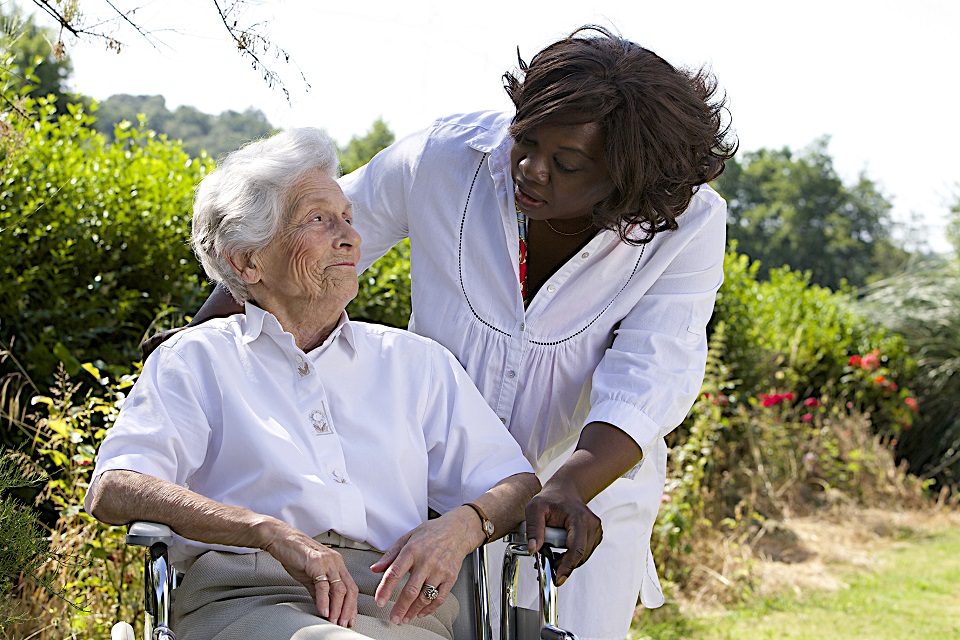 Afro-american caregiver talking to disabled senior woman outdoors